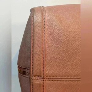 A close-up of the bottom corner of a pink leather bag, showing a stitched seam and textured leather.