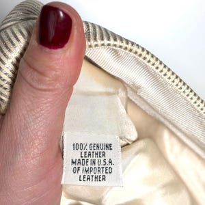 Close-up of a hand with dark red nail polish holding the interior material label that reads 100% genuine leather made in U.S.A. of imported leather.