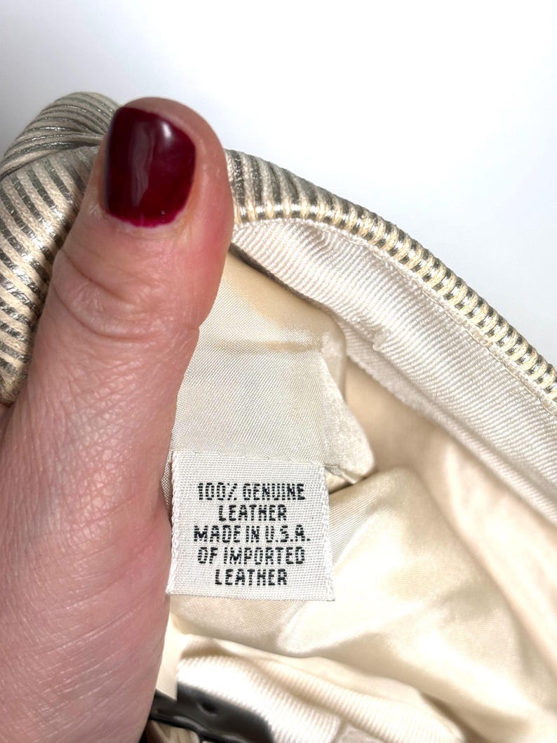 Close-up of a hand with dark red nail polish holding the interior material label that reads 100% genuine leather made in U.S.A. of imported leather.