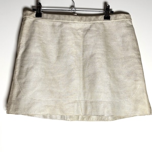 Front view of a cream-colored textured leather mini skirt hanging from a black clip hanger against a white background.