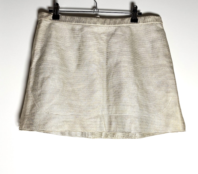 Front view of a cream-colored textured leather mini skirt hanging from a black clip hanger against a white background.