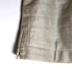 Close-up of the lower left hem and open side zipper on the textured cream leather skirt.