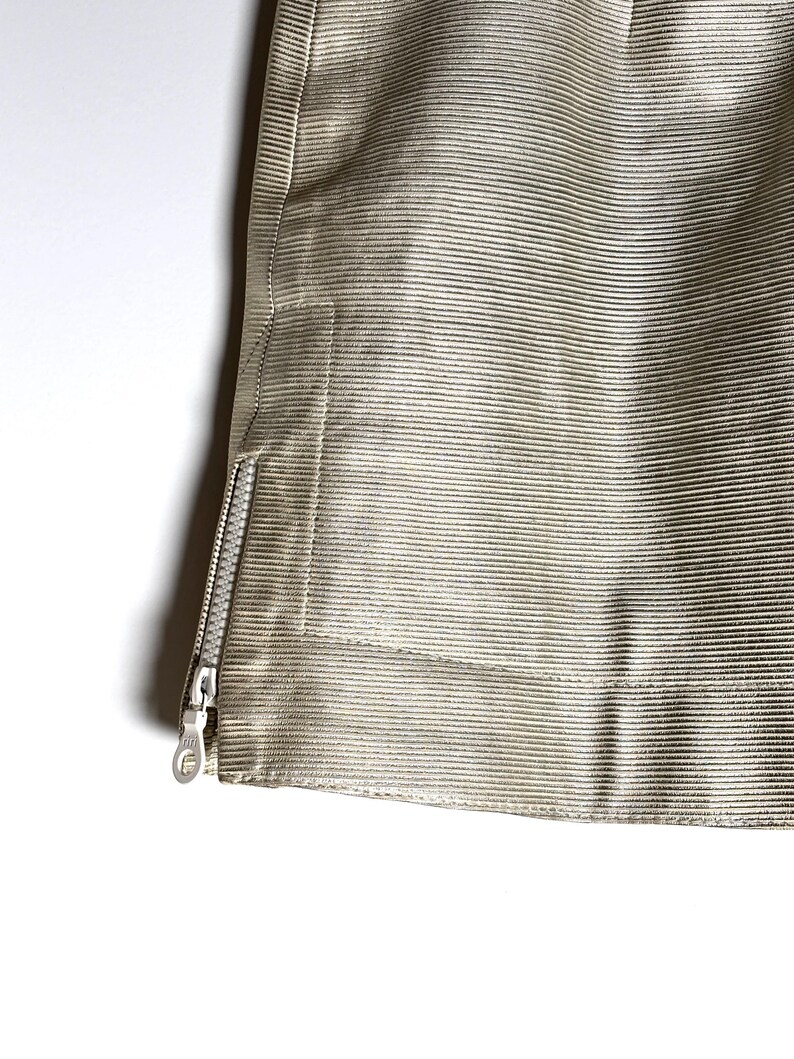 Close-up of the lower left hem and open side zipper on the textured cream leather skirt.