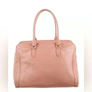 A pink leather handbag with two top handles, centered on a white background, with no charm visible.