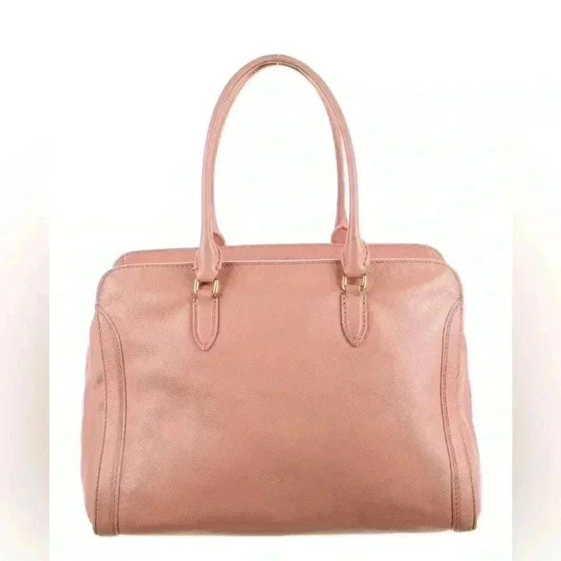 A pink leather handbag with two top handles, centered on a white background, with no charm visible.
