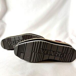 Underside view of the platform shoes displaying the ridged black rubber soles with the Prada logo embossed in the center.