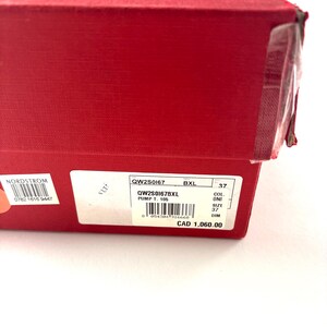 May include: A red shoe box with a white label displaying product information. The label includes the style number, size 37, and other details. The box is sealed with clear tape.