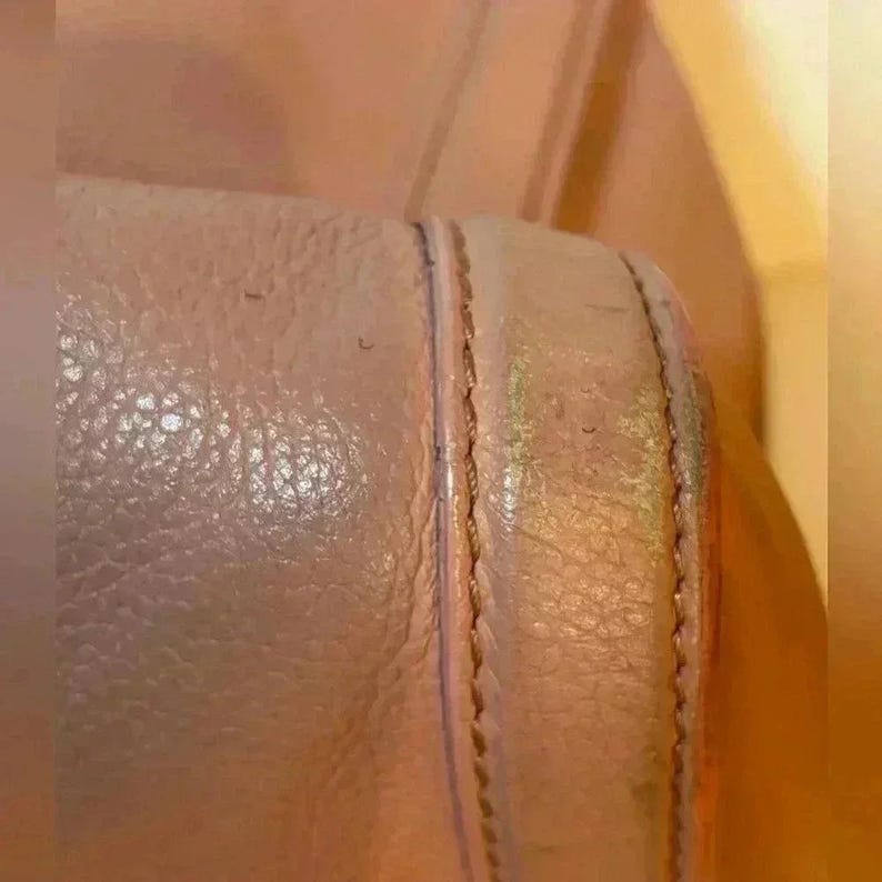 A close-up of a stitched seam on a pink leather bag, showing wear and discoloration along the edge.