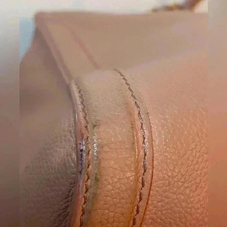 A close-up of the side seam of a pink leather bag, showing stitching and slight discoloration along the edge.
