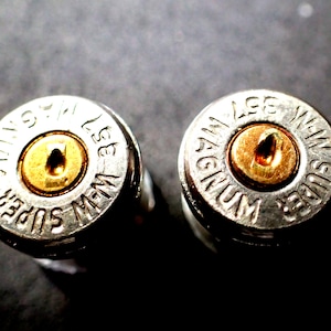 Op de afbeelding: Twee metalen .357 Magnum Super W-W hulzen. De hulzen zijn zilverkleurig met goudkleurige primers. De tekst "SUPER MAGNUM" en "357 W-W" is op de hulzen gegraveerd. De achtergrond is donker.