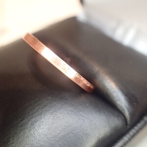 May include: A thin, rose gold band ring. The ring is sitting in a black velvet box.