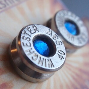 May include: A pair of silver bullet earrings with blue gemstones. The bullets are engraved with "Winchester" and "40 S&W".