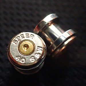 May include: A pair of silver bullet-shaped ear gauges with the text "SPEED 40 S&W" on one gauge.