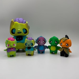 May include: A collection of colorful, stylized figurines. The figures include a zombie, a creature with tentacles, and a pumpkin-headed character. The figurines are painted in bright shades of green, blue, purple, and orange, with black accents.
