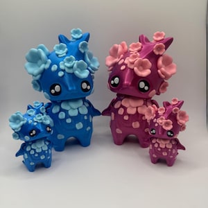 May include: Four whimsical figurines in varying sizes. Two are blue with light blue flower accents, and two are pink with pink flower accents. Each figure has large, round eyes and a spotted pattern on its body.