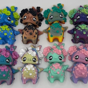 May include: A collection of twelve colorful, whimsical figurines. Each figurine has a unique color scheme, including blue, brown, green, purple, and pink. They feature flower-like details on their heads and bodies, with large, expressive eyes.