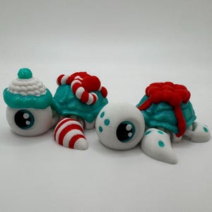 May include: Four whimsical, white-eyed turtle figurines with teal shells and decorative elements. One has a cupcake-shaped top, another has candy canes, and a third has a red bow. The fourth turtle has a red, volcano-like top.