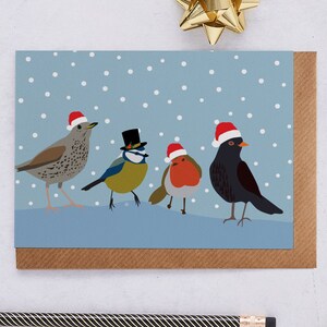 Carte de Noël avec des oiseaux chanteurs, avec une grive musicienne, un rouge-gorge et un merle en bonnets de Noel et une mésange bleue en haut de forme