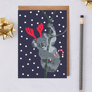 Koala di Natale Katie indossa corna rosse di renna di Natale e tiene in mano un bastoncino di caramelle
