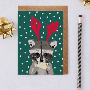 Christmas raccoon card wearing red reindeer antlers and holding letter