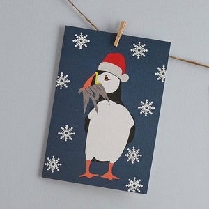 Macareux moine de Noël portant un bonnet de Noel avec un poisson en cadeau pour ses amis et sa famille.