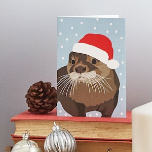 Cartão de lontra de Natal usando um chapéu de Papai Noel