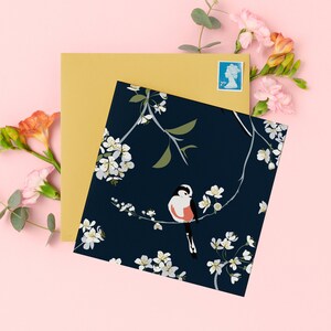 Cartão azul marinho com flores e pássaros, chapim-rabo-longo contra um fundo azul marinho e flor de macieira britânica