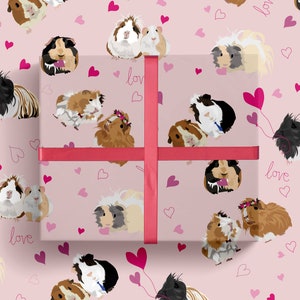 May include: Pink wrapping paper with a repeating pattern of guinea pigs and hearts. The guinea pigs are in various poses, some are holding hearts, and some are wearing crowns. The text "love" is repeated throughout the pattern.