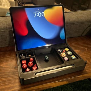 May include: A black tray with compartments for dice and a stylus. The tray is open and a tablet is in the top compartment. The tablet screen shows the time as 7:00 and the date as Monday, March 3.