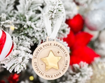 Puede incluir: Un adorno redondo de madera con una estrella dorada y el texto "North Pole Approved Official Nice List Award".
