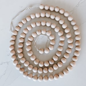 Op de afbeelding: Een lange streng natuurlijke houten kralen aan elkaar geregen met een wit touwtje. De kralen zijn allemaal even groot en hebben dezelfde vorm, en ze zijn in een cirkelvormige patroon gerangschikt.