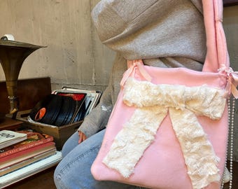 Peut inclure: Un sac cabas rose avec un grand nœud en fausse fourrure blanche. Le sac a une bandoulière en chaîne de perles.