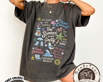 May include: Dark gray t-shirt with a graphic design featuring summer-themed illustrations and text. The design includes phrases like "The Summer I turned Pretty," "Team Conrad," and "Cousins Beach." The shirt also has the words "Comfort Colors" and "Pepper" printed on it.