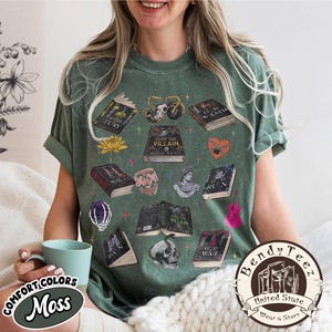 May include: Moss green t-shirt with various book illustrations, a motorcycle, a skull, and other graphics. The shirt features the text "HUNT THE VILLAIN" and "KISS THE VILLAIN". The shirt also has the text "COMFORT COLORS Moss" and "Bendy Tee United State Wear a Story".