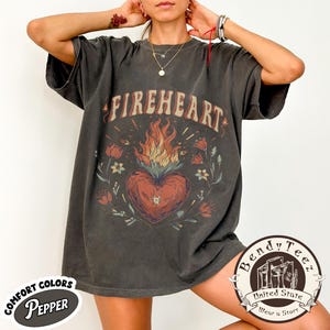 May include: Dark grey t-shirt featuring the word "FIREHEART" above a heart-shaped flame design. The design includes floral elements and the text "COMFORT COLORS Pepper" and "Bendy Teez United State Wear a Story".