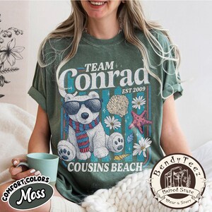 May include: Green t-shirt with a graphic of a polar bear wearing sunglasses and a scarf, with the text "Team Conrad EST 2009 Cousins Beach". The shirt also has seashell and starfish graphics.