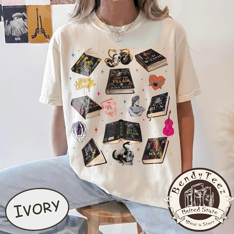 May include: Ivory-colored t-shirt featuring various book illustrations, including titles like "Hunt the Villain" and "God of Ruin." The design incorporates skulls, a violin, and other gothic-themed elements. The shirt also has the text "Bendy Teez" and "Wear a Story."