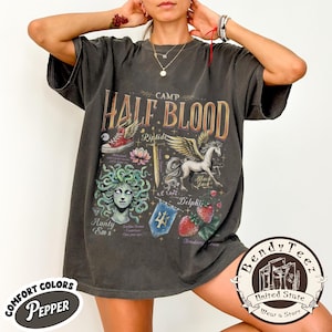 May include: Dark gray t-shirt with the text "CAMP HALF BLOOD" and various illustrations including a winged horse, strawberries, and a sword. The shirt also features the text "COMFORT COLORS PEPPER".