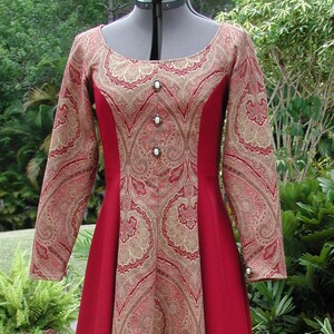May include: A long red dress with a paisley pattern in gold and red. The dress has a scoop neck and long sleeves. The dress is made of a soft, flowing fabric.