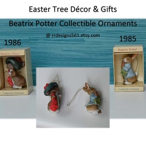 May include: Two Beatrix Potter collectible ornaments in their original boxes. The ornament on the left is a mouse wearing a green hat and red dress. The ornament on the right is a rabbit wearing a blue jacket and holding a carrot. The boxes are white with gold trim and feature the Beatrix Potter logo. The text on the boxes reads "Beatrix Potter Collectible Ornament" and the year "1986" or "1985".