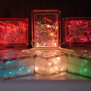 May include: Five rectangular glass blocks arranged in two rows, each containing strings of glowing LED lights. The top row features red and multi-colored lights, while the bottom row displays blue, warm white, and green lights inside the clear glass.