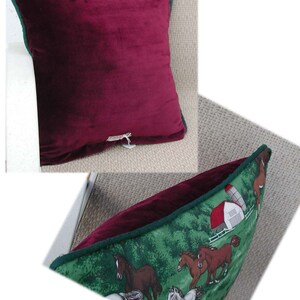 May include: A square throw pillow featuring a solid deep burgundy velvet front and a green back panel decorated with a printed scene of horses running in a field near a white barn with a red roof. The pillow is finished with dark green piping.