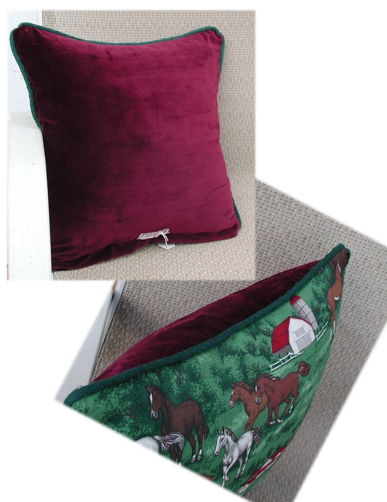 May include: A square throw pillow featuring a solid deep burgundy velvet front and a green back panel decorated with a printed scene of horses running in a field near a white barn with a red roof. The pillow is finished with dark green piping.