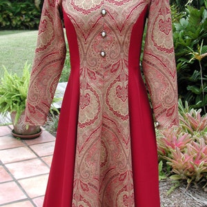 May include: A long-sleeved red dress with a gold paisley pattern. The dress has a scoop neckline and a fitted bodice. The skirt is full and flowing. The dress is adorned with pearl-like buttons.