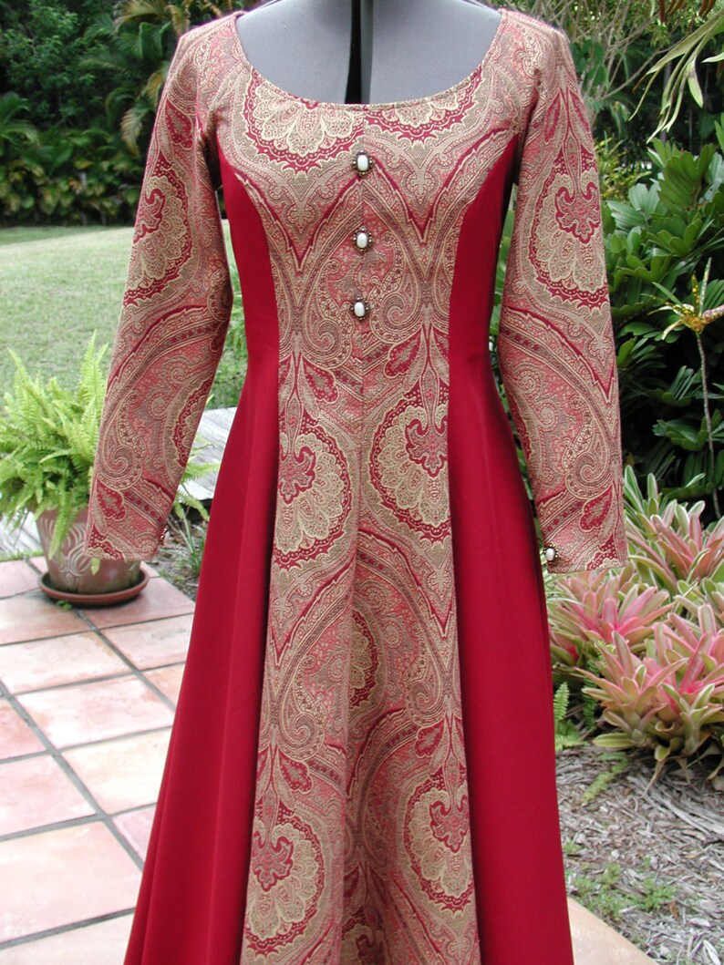 May include: A long-sleeved red dress with a gold paisley pattern. The dress has a scoop neckline and a fitted bodice. The skirt is full and flowing. The dress is adorned with pearl-like buttons.