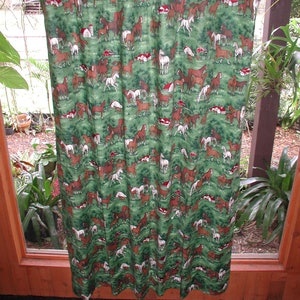 May include: A green fabric curtain featuring a repeating pattern of brown, white, and black horses in a field with small red barns. The curtain is suspended from a horizontal wooden rod by several circular brown rings along the top edge.