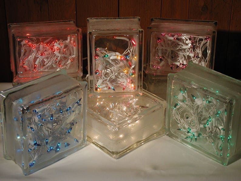 May include: A collection of five rectangular glass blocks, each containing a string of miniature electric lights. The lights inside the blocks glow in various colors, including red, blue, green, and multi-colored, with white wiring visible.