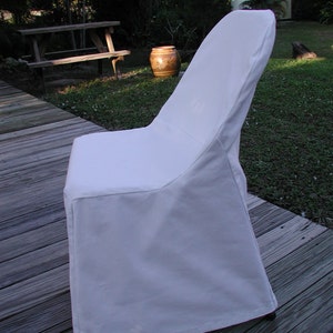 May include: A white folding chair with a simple design. The chair is made of a soft, white fabric and has a padded seat. The chair is sitting on a wooden deck.
