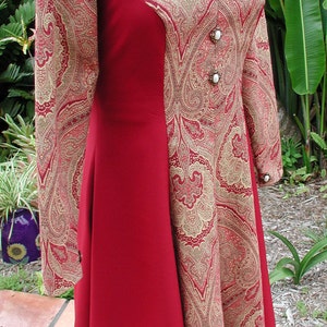 May include: A red and gold paisley patterned dress with a fitted bodice and a flowing skirt. The dress has a scoop neckline and three white buttons down the front.