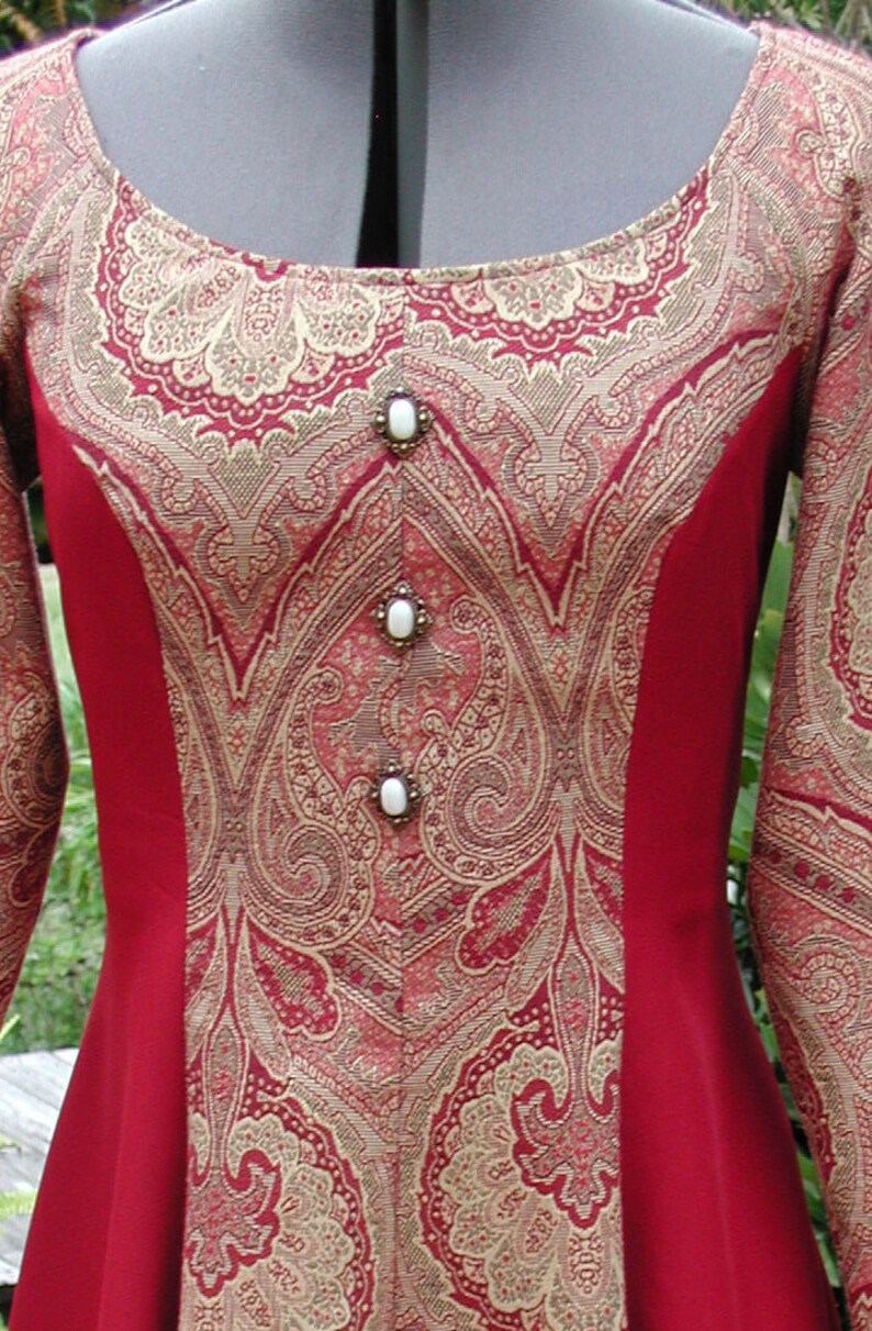 May include: A red dress with a gold and red paisley pattern. The dress has a scoop neckline and long sleeves. The dress is decorated with four white buttons.